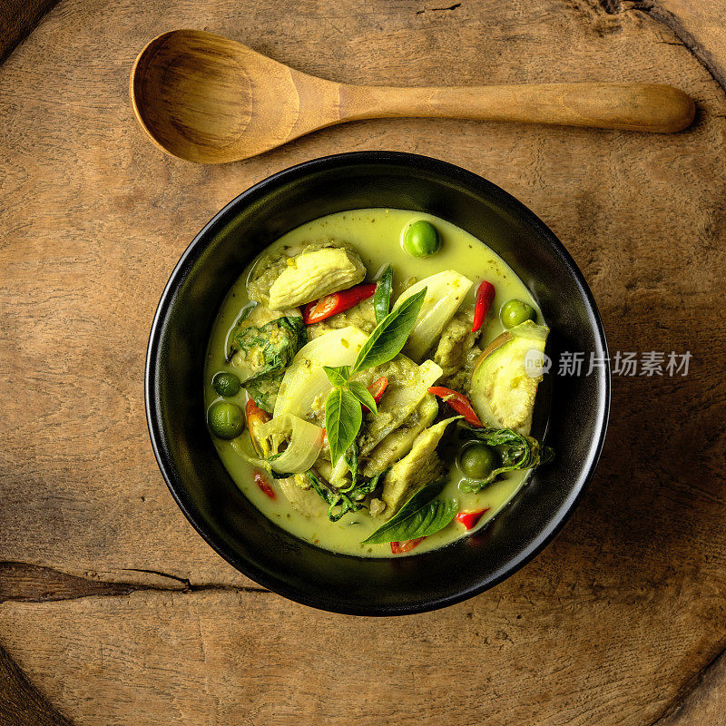 著名的国际知名的泰国绿色椰子咖喱“Gaeng Keow Wan Gai”，鸡肉，放在碗里，放在一个破旧的木托盘上，碗边有一个木勺子。